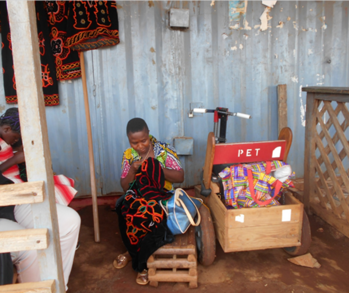 Picture of Nina in front of her shop, embroidering a dress for a customer, copyrigts Cameroon Baptist Convention Health Services