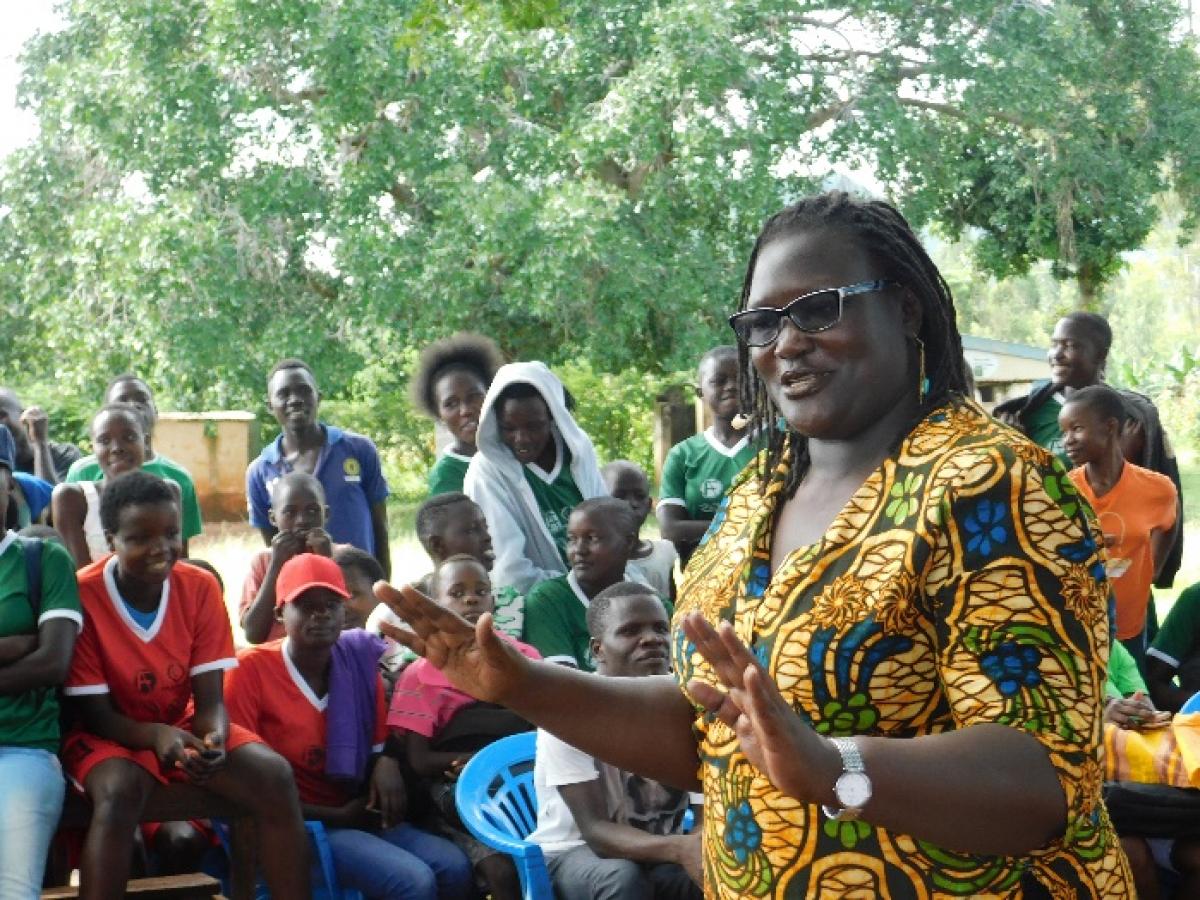 Easter Okech speaking at “Sports for change” SRHR conversations, with a group of people listening in the background.