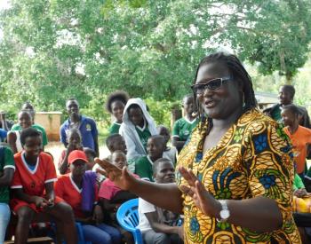 Easter Okech speaking at “Sports for change” SRHR conversations, with a group of people listening in the background.