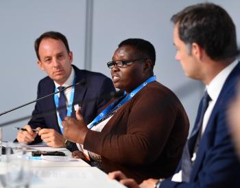 Photo de Jane Kihungi s'exprimant lors des Journées européennes du développement 2018, avec l'actuel Premier ministre De Croo à sa gauche, crédit EDDs.